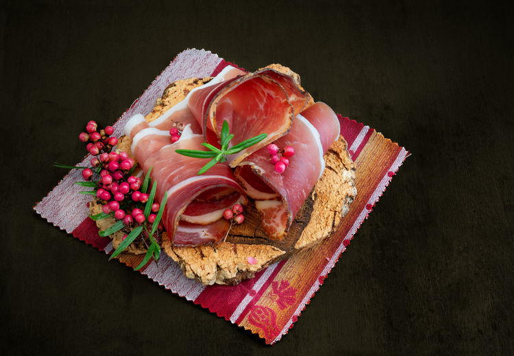 Slices of alto adige speck rolled with wild red pepper on a cork plate