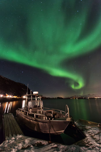 Boat moored at harbor with aurora in sky at night