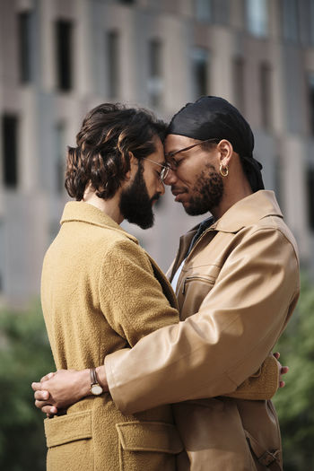 Gay couple with eyes closed embracing each other outside building