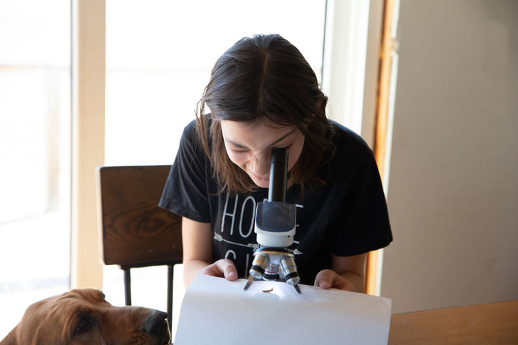 Tween girl looking into microscope with dog looking on