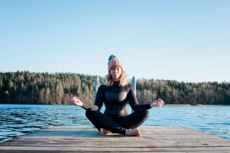 Woman meditating in a wetsuit at the beach before cold water swimming