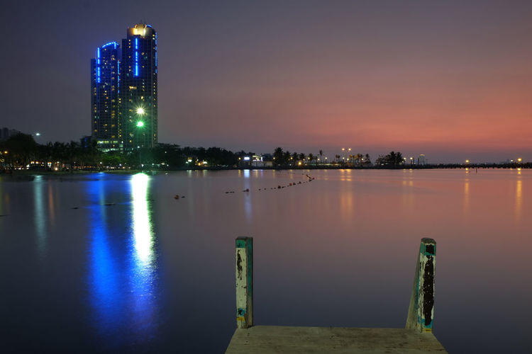 Scenic view of lake by illuminated buildings against sky at night