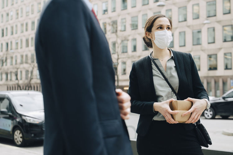 Female entrepreneur with boxes standing by male colleague in city during pandemic