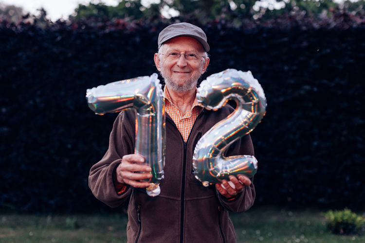 Smiling elderly man holding balloons with the number 72 on his birthday