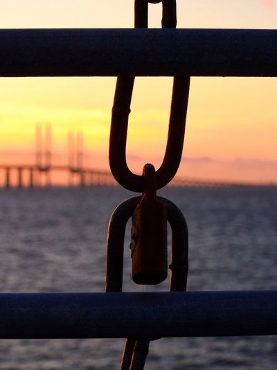 Close-up of metal railing against sea during sunset