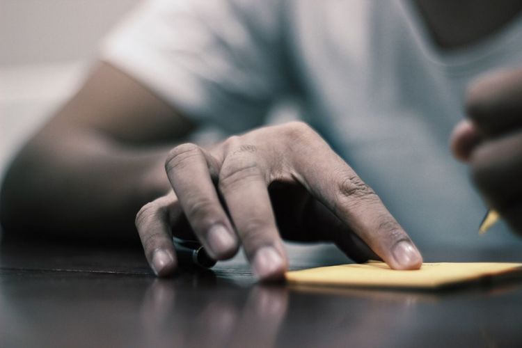 Midsection of man holding adhesive note on table
