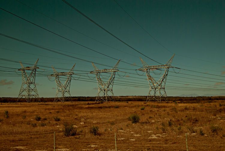 Electricity pylon on field against blue sky