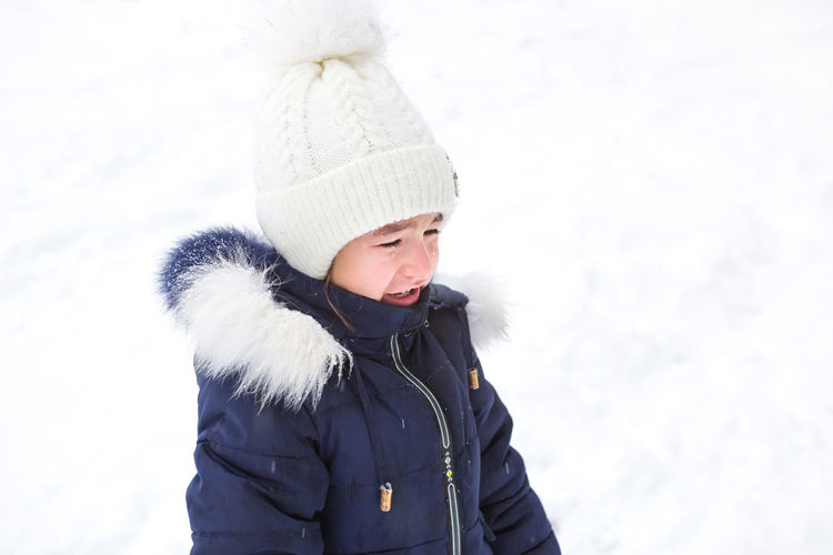 Little girl crying outside in winter. a child in warm clothes is upset, cold, wipes away tears, 