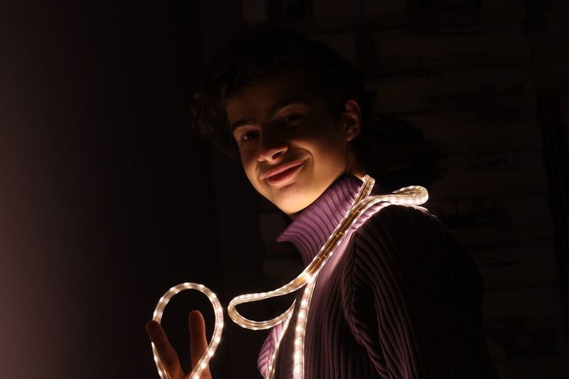 Portrait of smiling teenage boy with illuminated strip light against black background