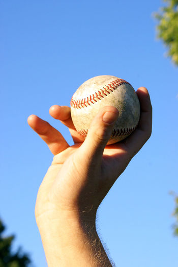 Low angle view of hand holding baseball against sky