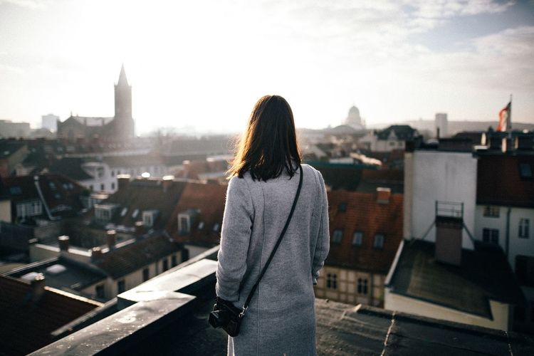 Rear view of woman standing by cityscape against sky
