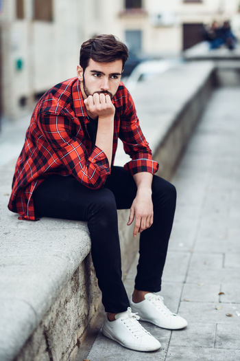 Full length of young man sitting on retaining wall