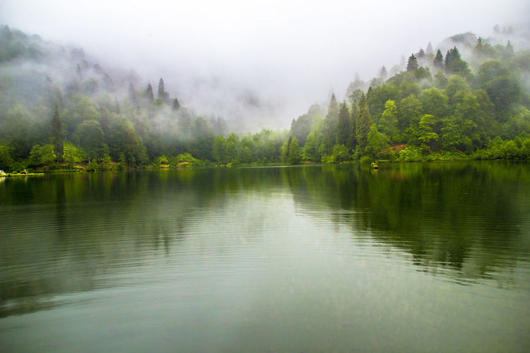Scenic view of lake by mountains in foggy weather