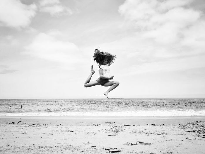 Girl jumping at beach against sky