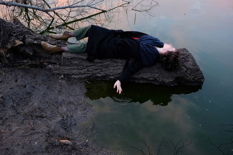 Full length of woman lying on fallen tree trunk by lake