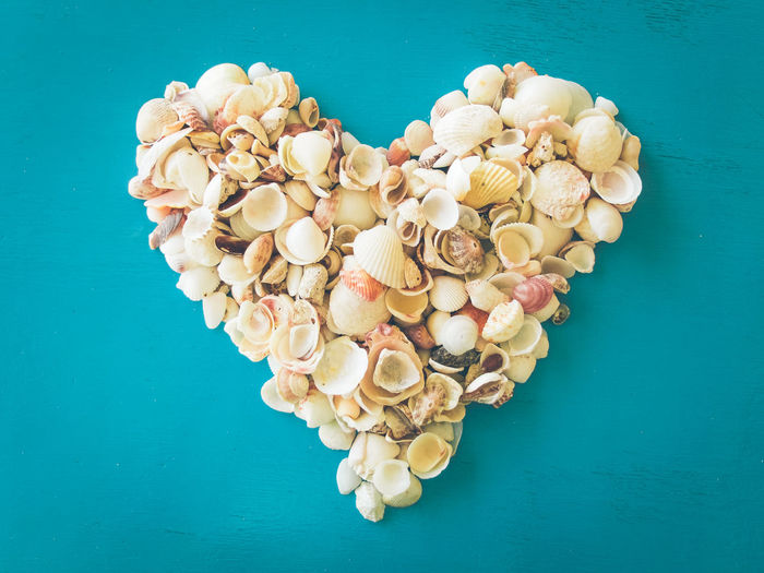 Directly above shot of heart shape made by seashells on blue table
