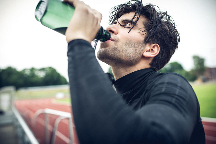 Close-up of athlete drinking water from bottle on sports track