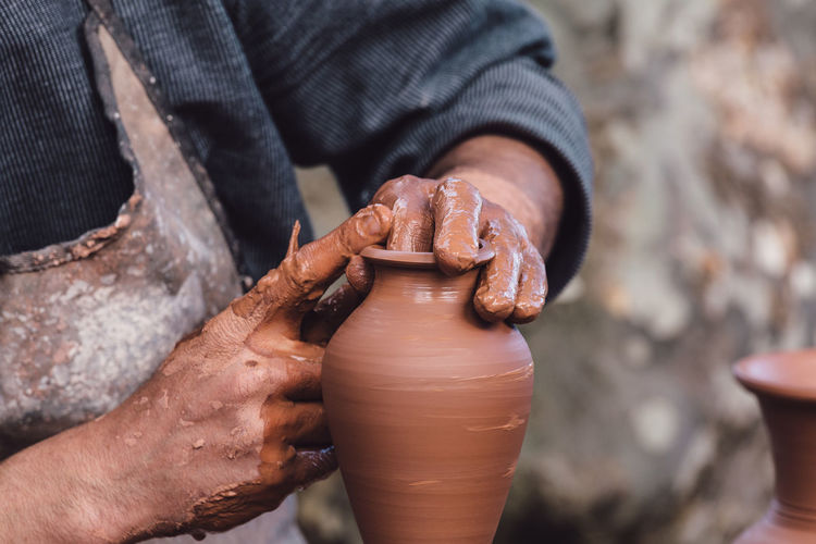 Cropped hands of potter making clay pot at pottery