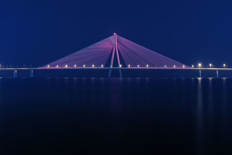 Illuminated bridge over sea against sky at night