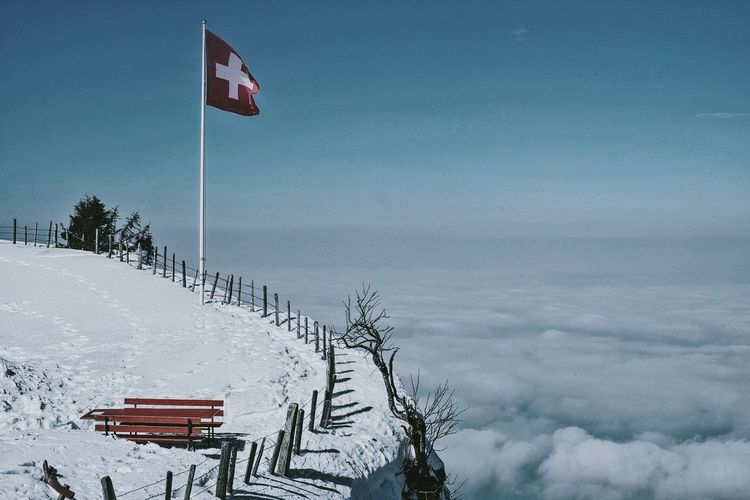 Swiss flag on mountain by cloud covering landscape