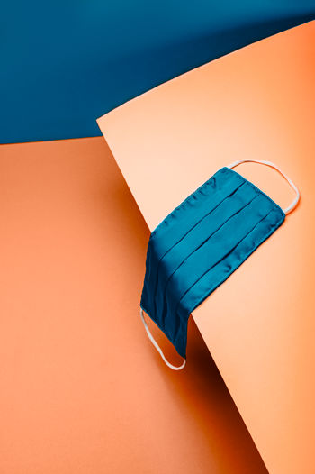 New normal with reusable protective silk face mask on blue and orange background, . trendy setting