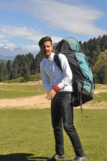 Full length of a young guy looking at camera with carrying parachute backpack in the mountain 