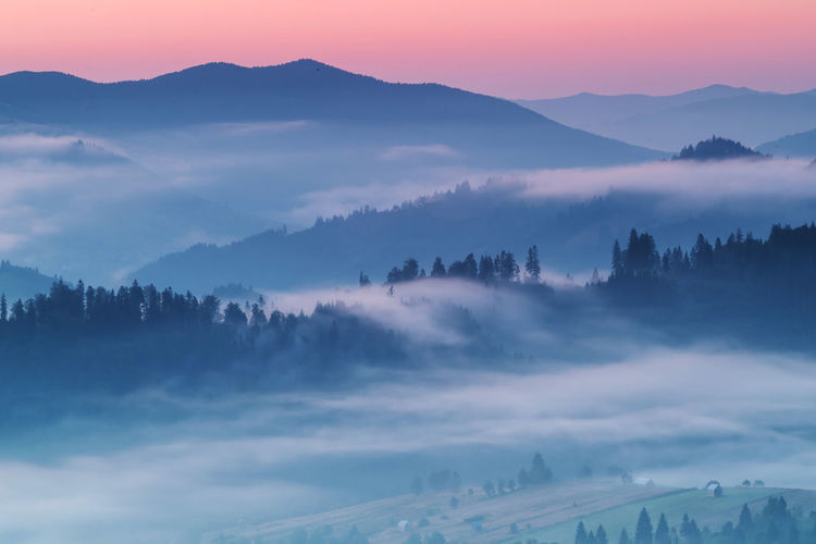Scenic view of mountains in foggy weather against sky during sunset