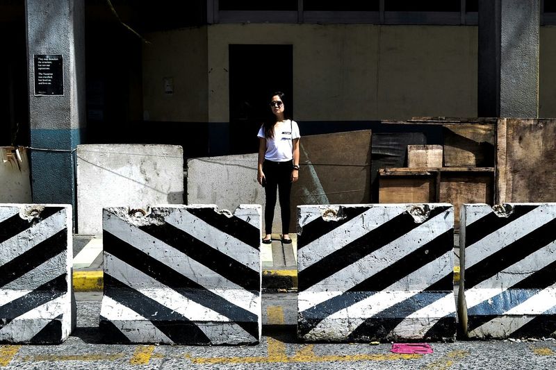 Full length of woman standing by barricade on street during sunny day