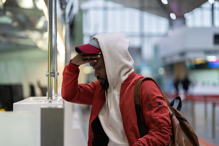Sad african man standing near check-in desk feeling frustrated because of flight cancellation