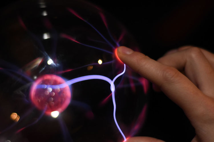 Cropped hand touching plasma ball against black background