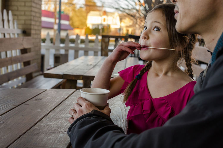 A happy girl enjoys a cup of cocoa with her father in an outdoor cafe
