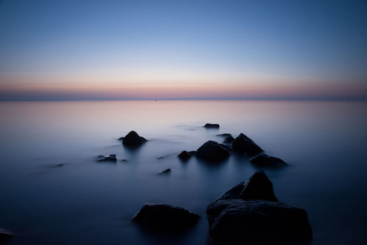 Rocks in sea against sky at sunset