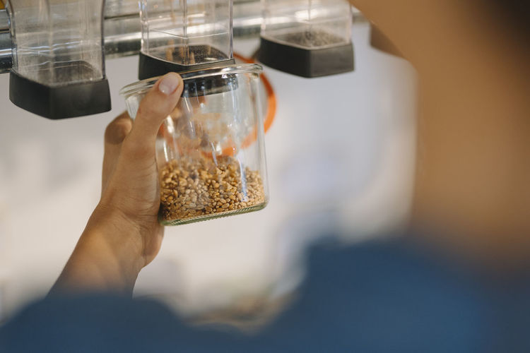 Cropped hand of female owner filling grain in jar while standing in cafe