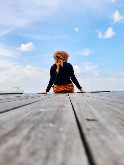 Woman sitting on pier against sky