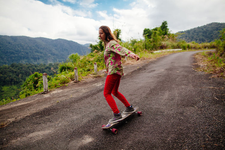 Woman skateboarding on road against cloudy sky
