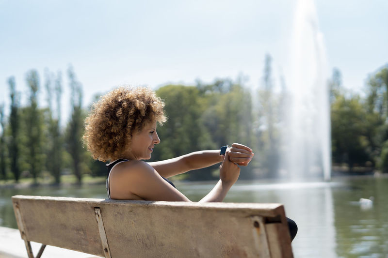 Woman on a bench by the lake using her smartwatch