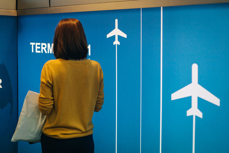 Rear view of woman standing against blue wall at airport terminal