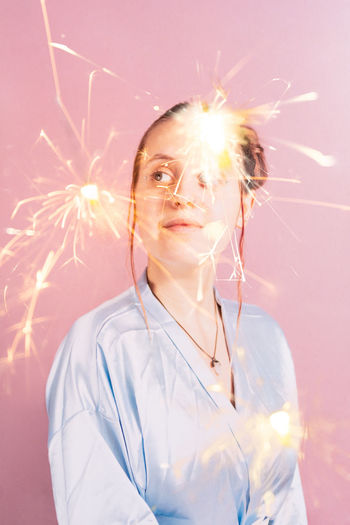 Digital composite image of thoughtful young woman and sparks against pink background