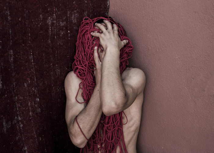 Shirtless man covering him with strings against wall