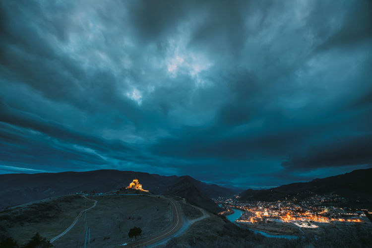 Aerial view of illuminated town by mountain against sky