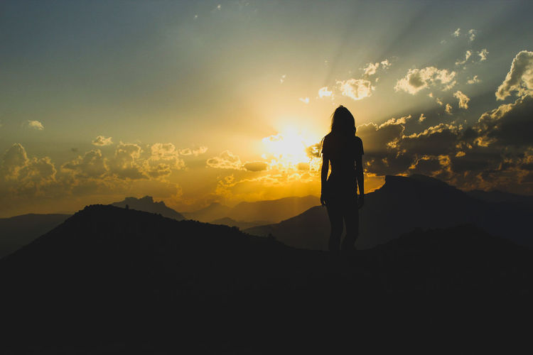 Silhouette woman standing on mountain against orange sky