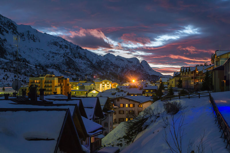 Houses and snowcapped mountains against sky during sunset