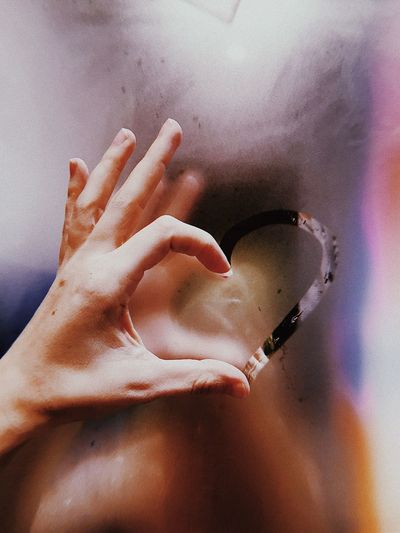 Cropped hand of person forming heart shape on window