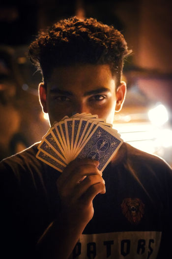 Close-up portrait of young man holding playing cards at night
