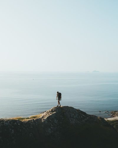 Man standing on rock by sea against clear sky