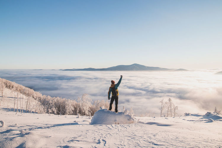 Man walking on snow covered landscape against clear sky