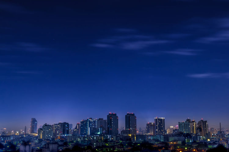 Illuminated buildings against blue sky at night