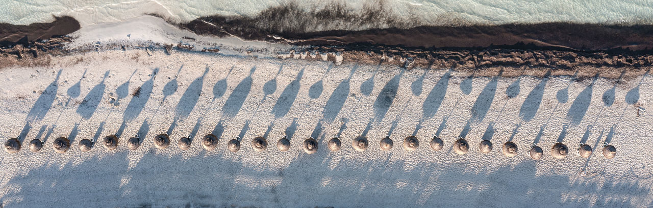 Lined up umbrellas seen from the air casting shadows over the white sand beach of es trenc, majorca
