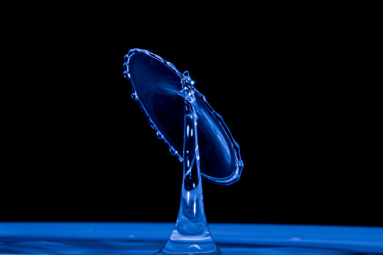 Close-up of water splashing glass against black background