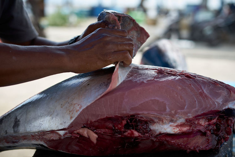 Fish vendor skinning fresh raw tuna fish at seafood market